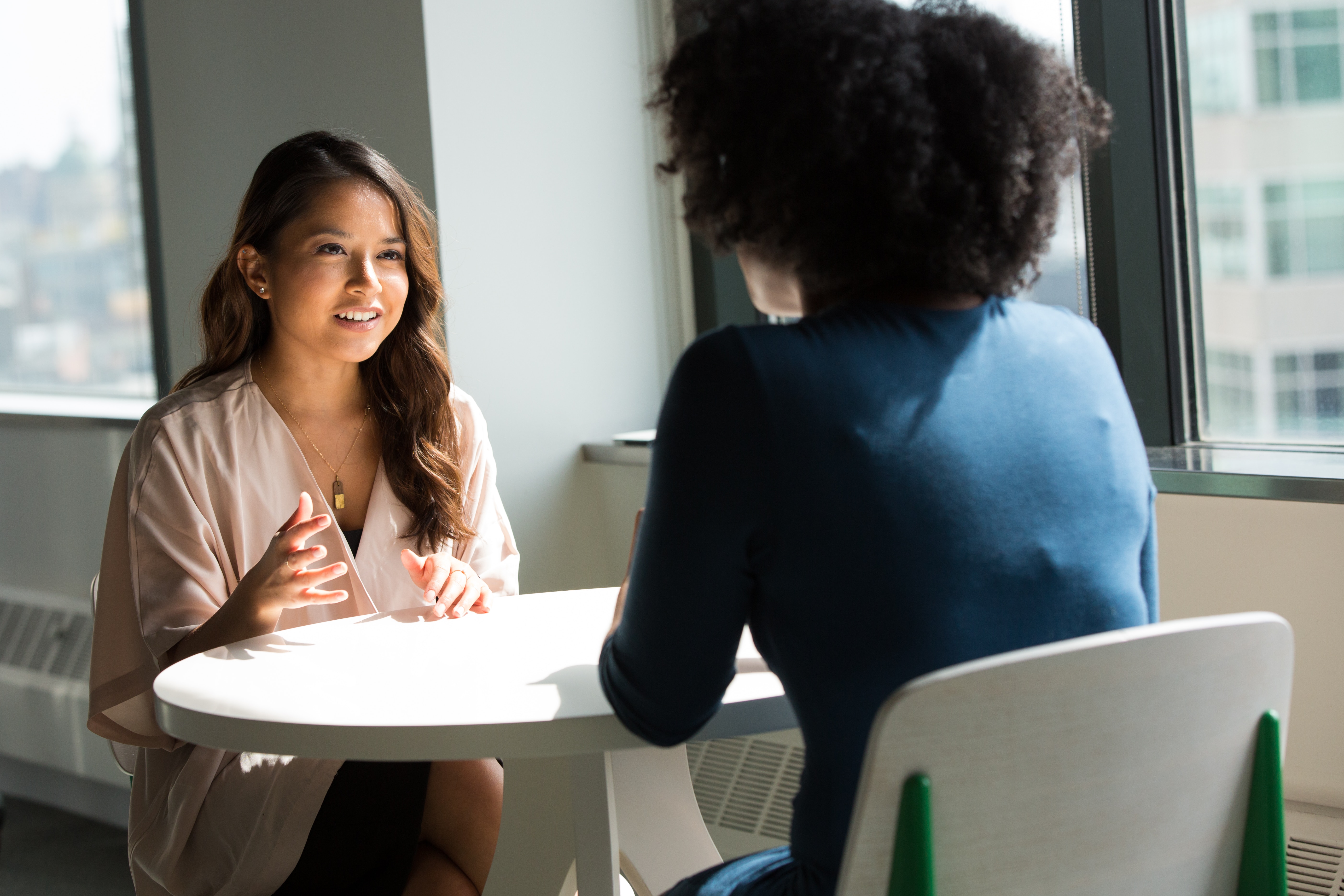 Two woman sat opposite each other a small table having a conversation