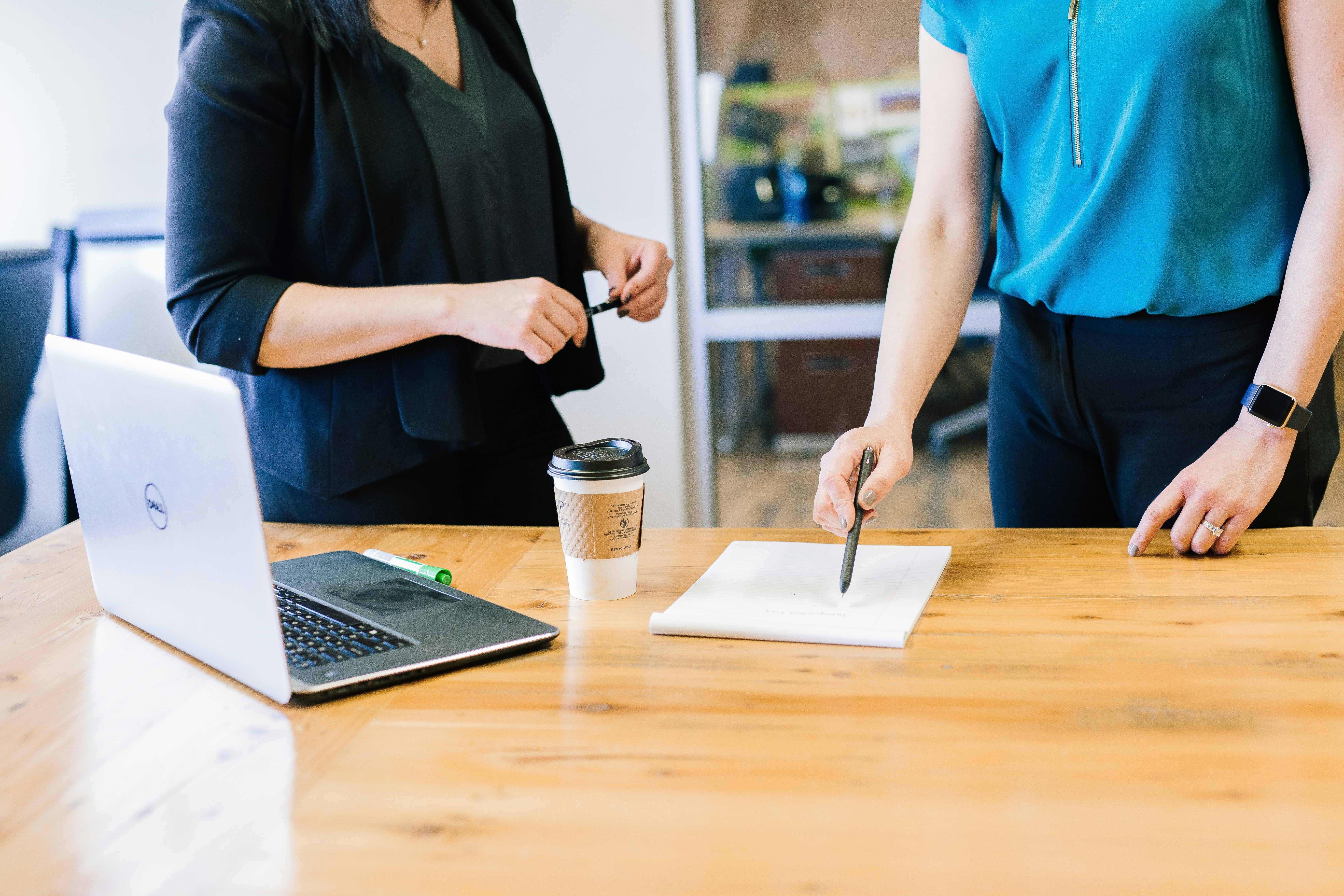 Two women looking at a piece of paper next to a laptop and cup of coffee