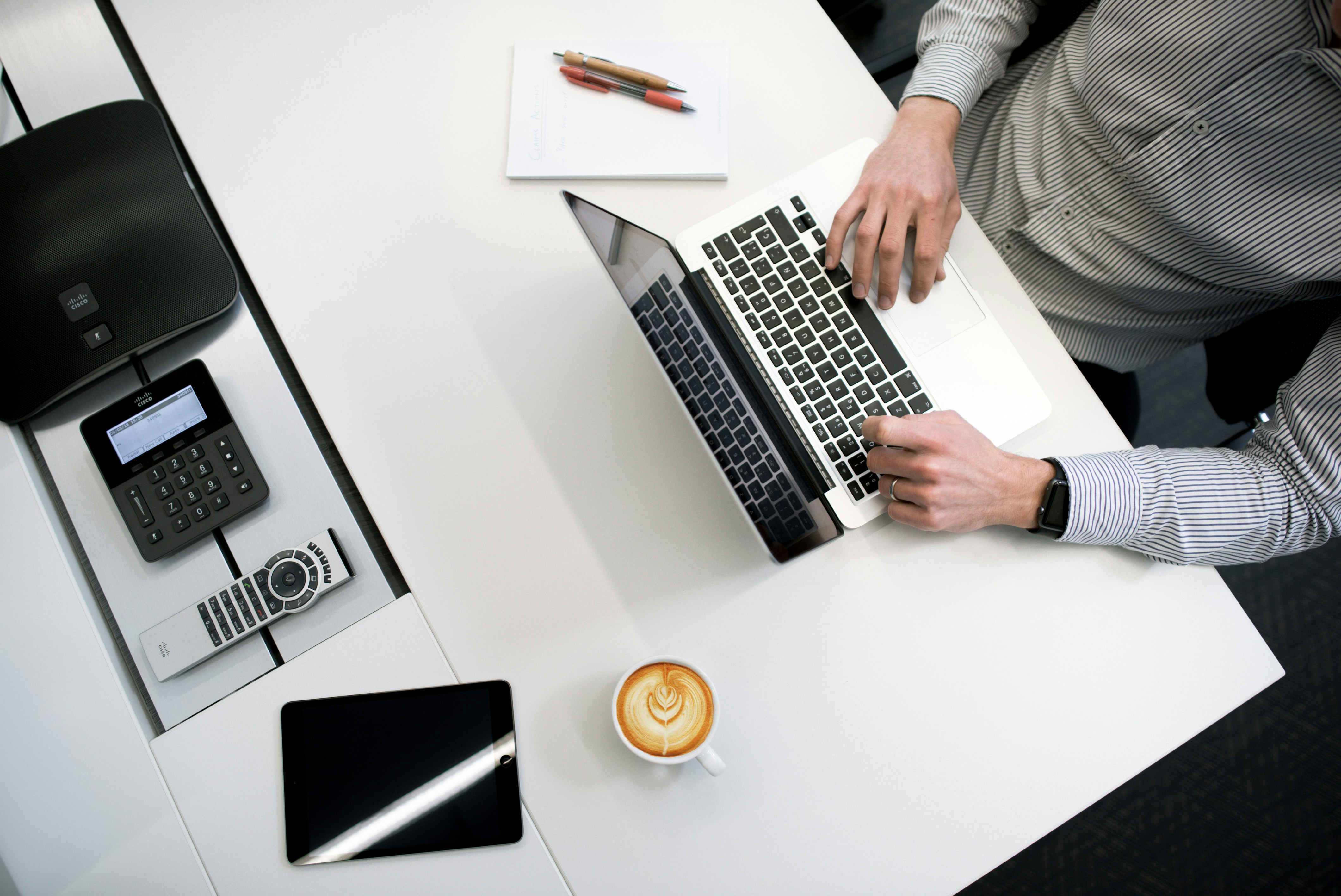 Man at desk typing on laptop, next to pens and paper 