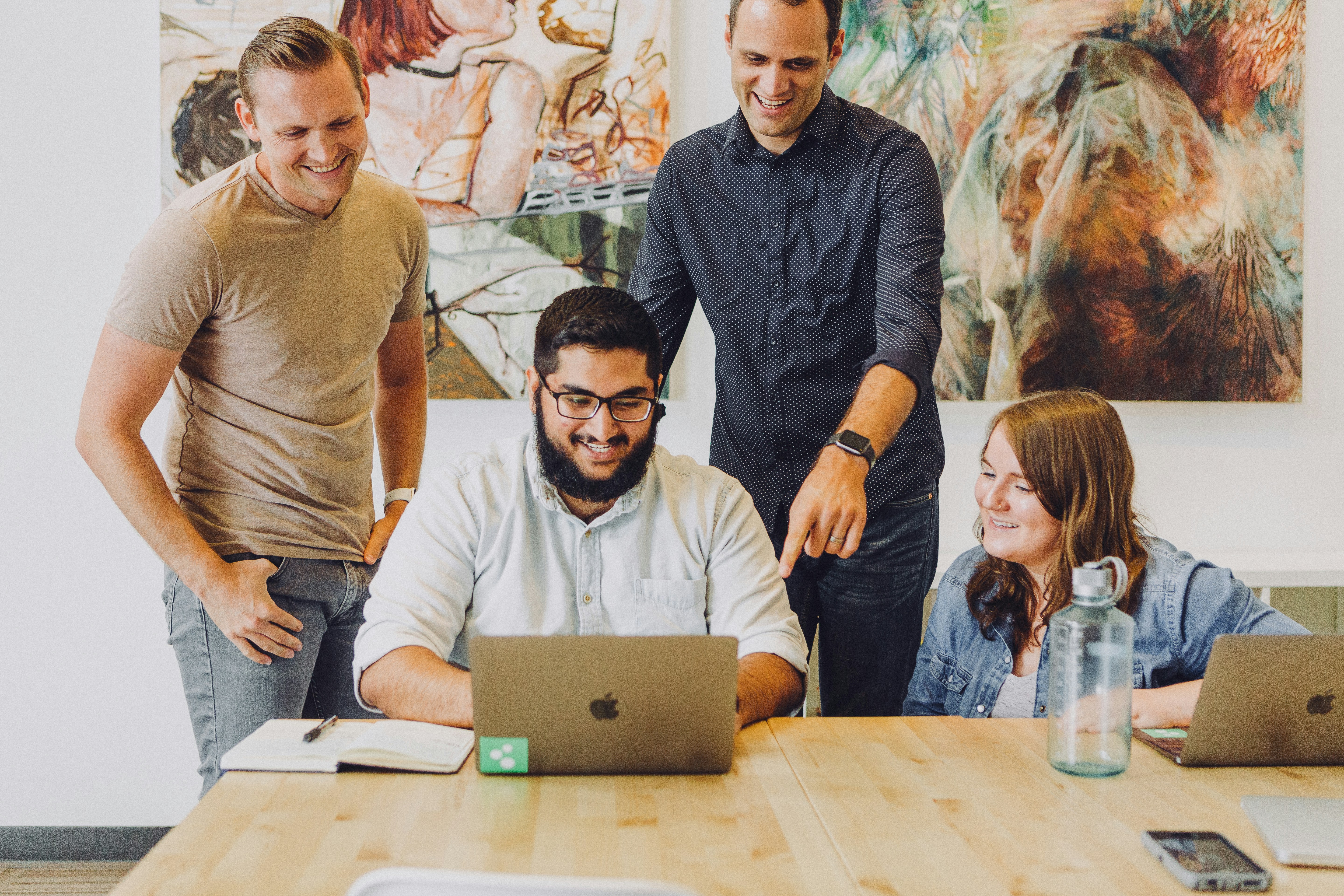 A group of 4 people looking at a laptop screen and smiling