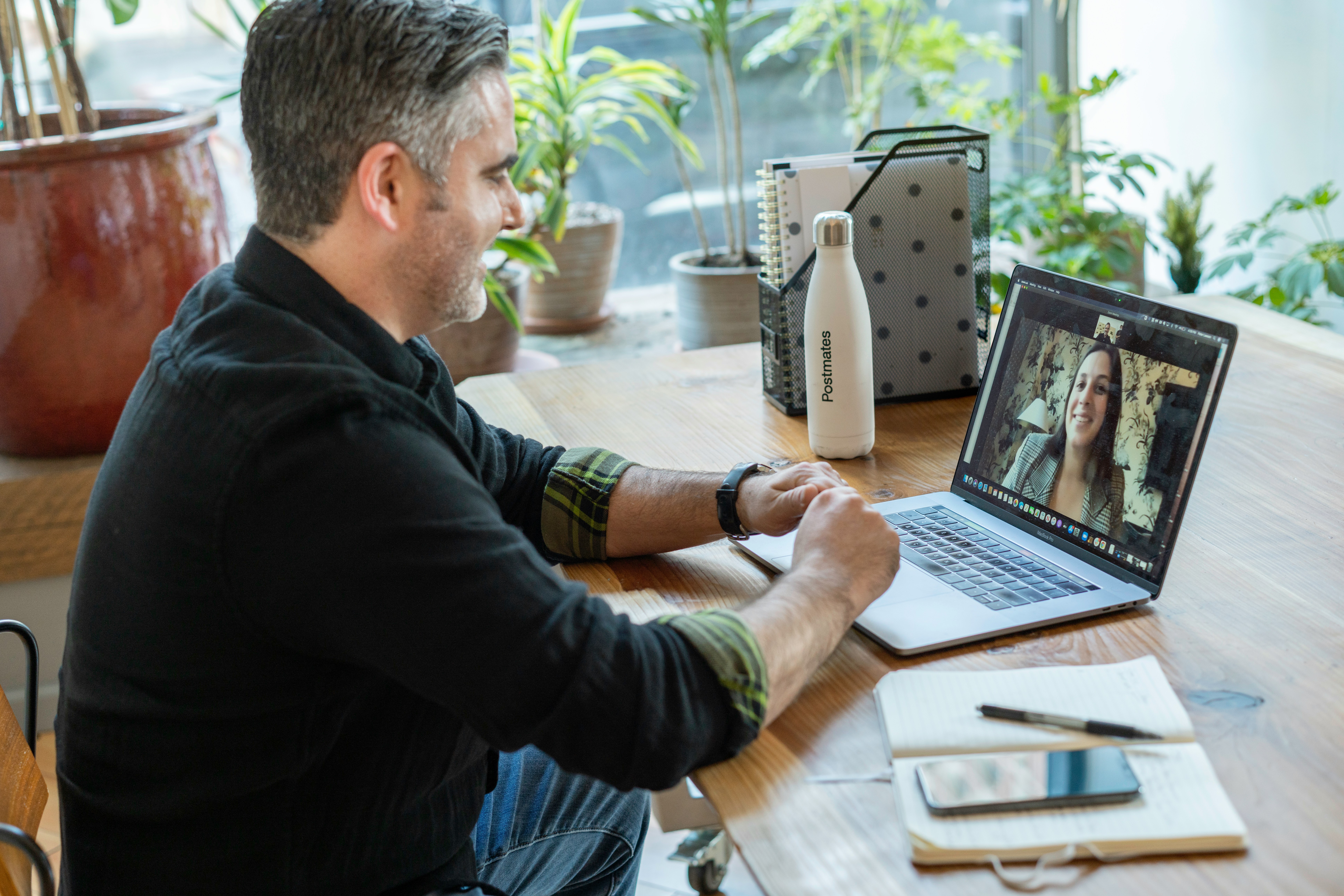 A man having a video call on a laptop with a woman next to a Postmates water bottle
