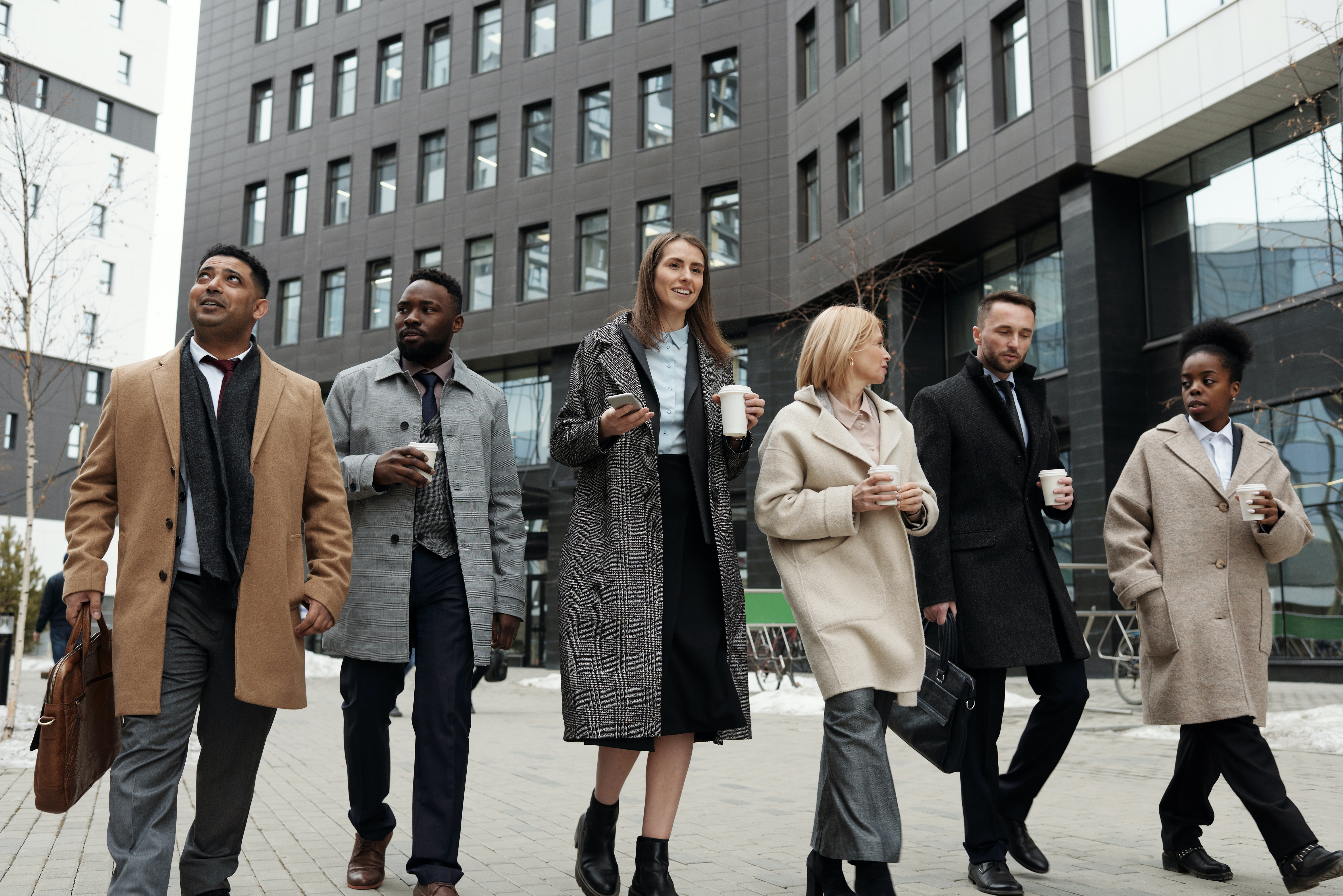 Group of 6 people in business dress and coats walking outside office building