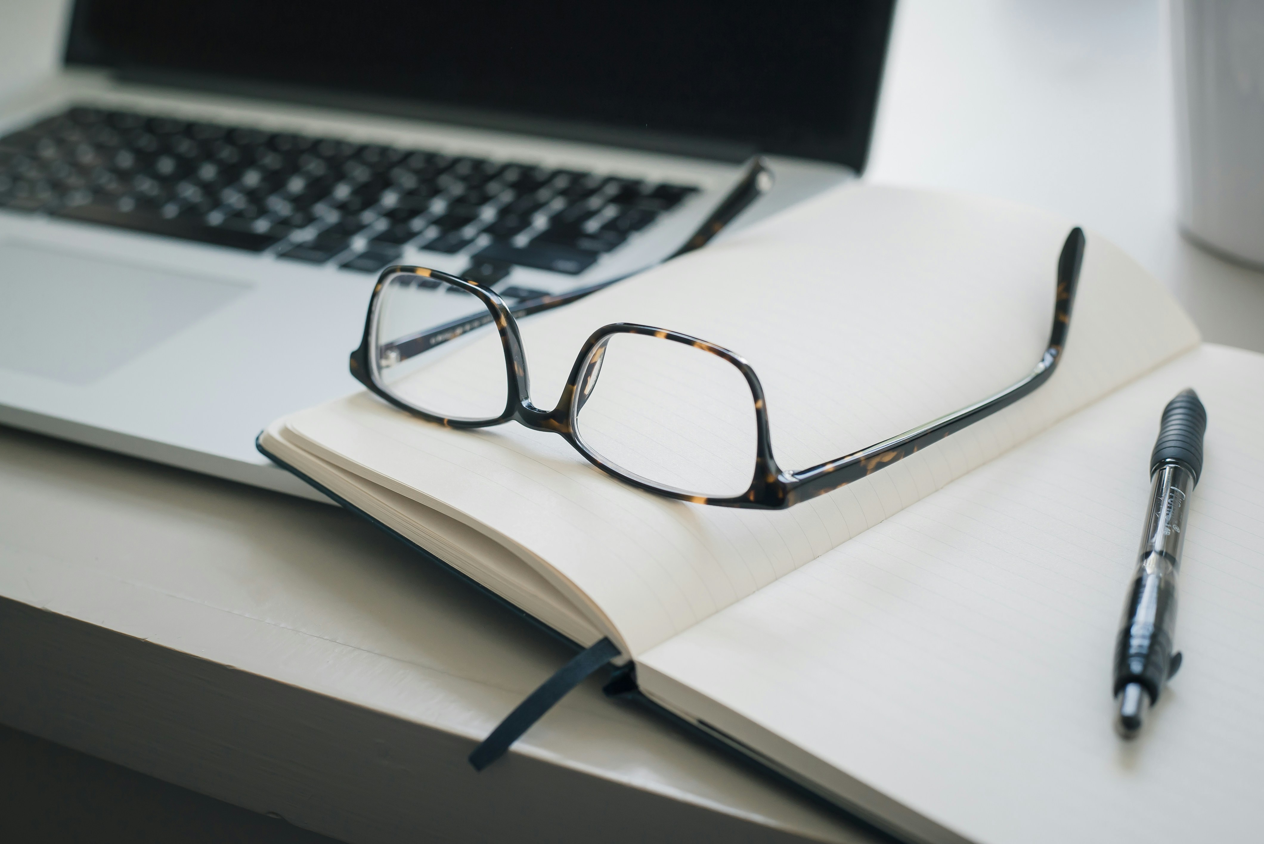 Close up on glasses and notepad next to a computer 