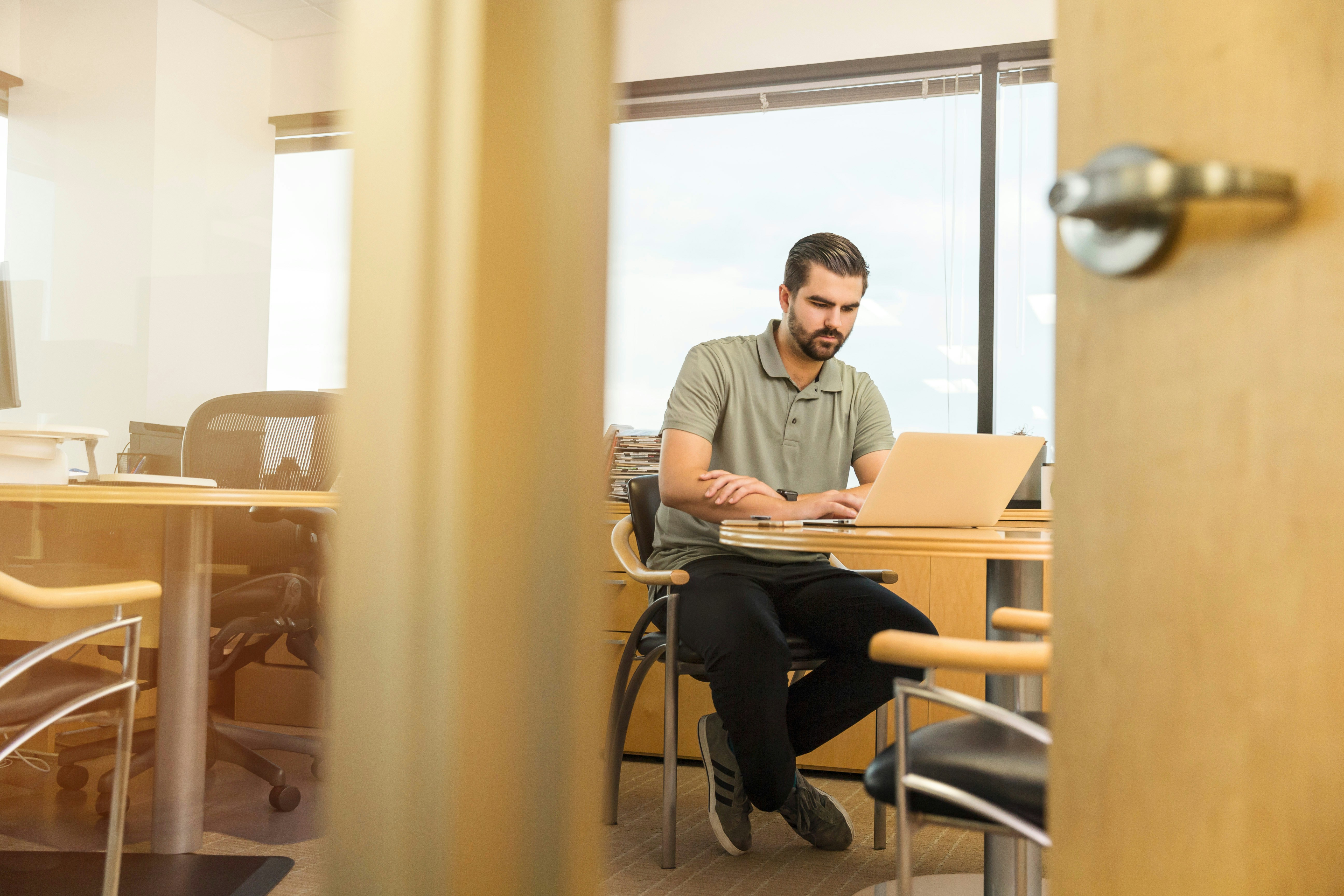 Man in office setting sat at a table looking at laptop