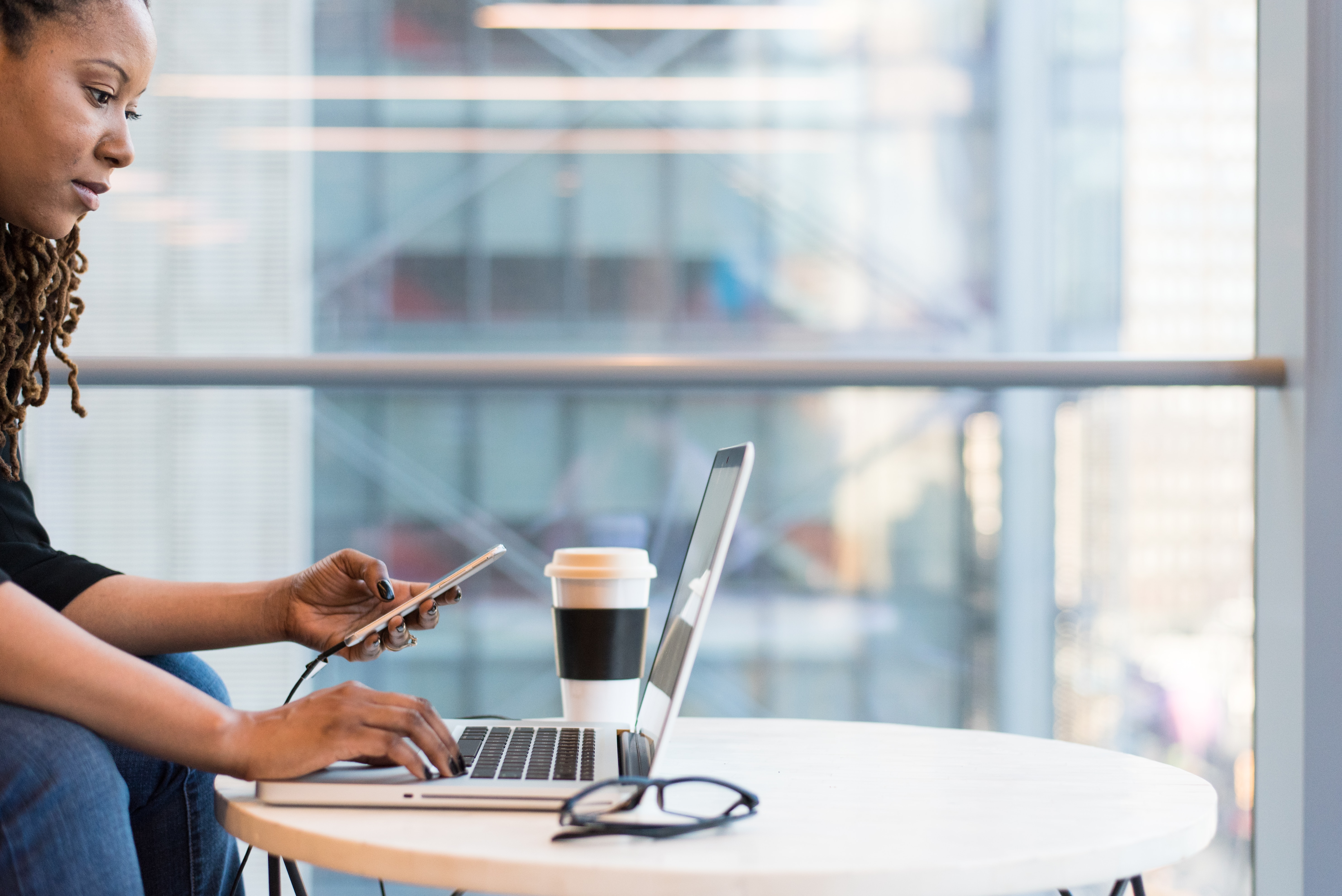 Female hands on laptop and mobile phone in office setting, next to a cup of coffee