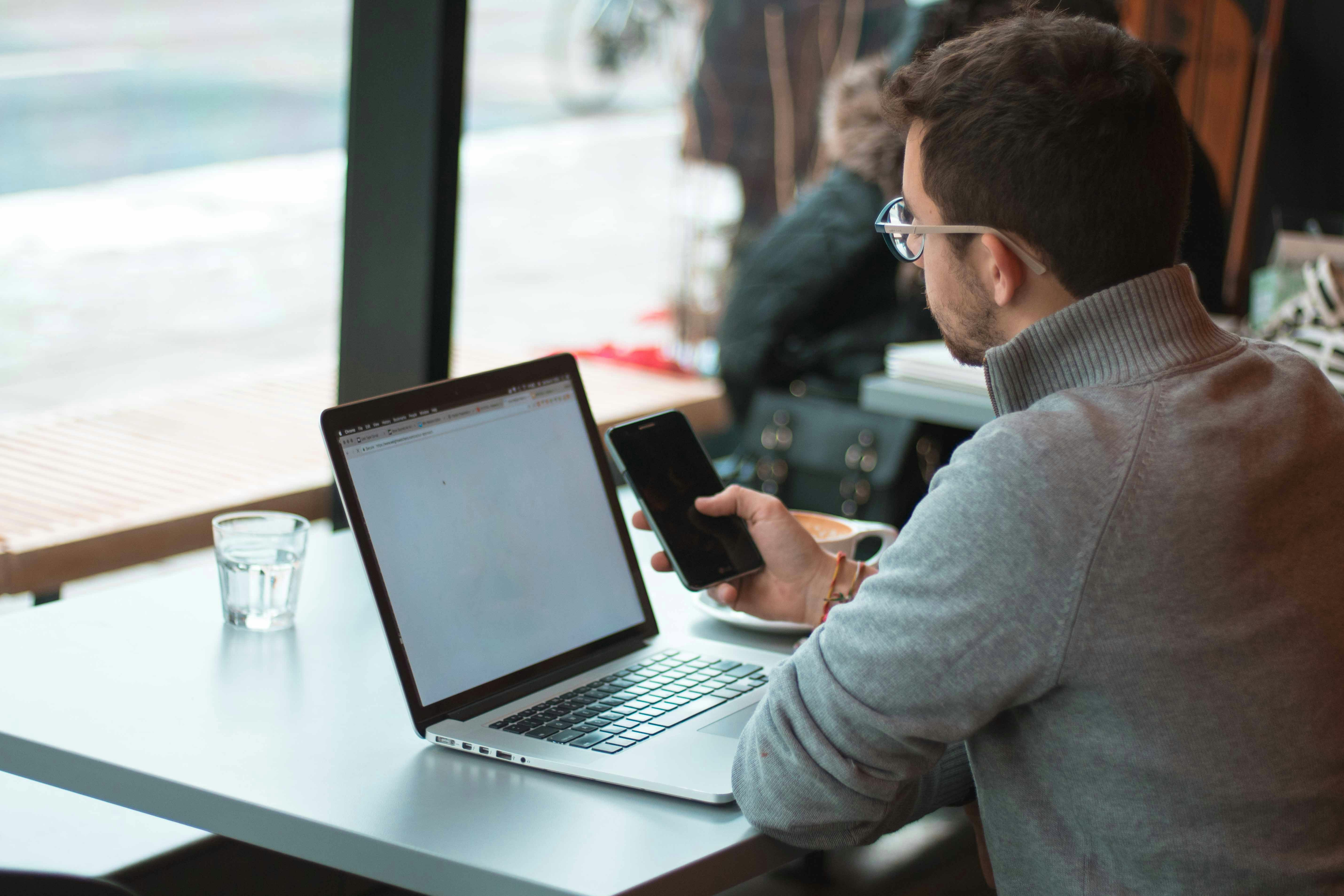 Man using mobile phone sitting in front of laptop