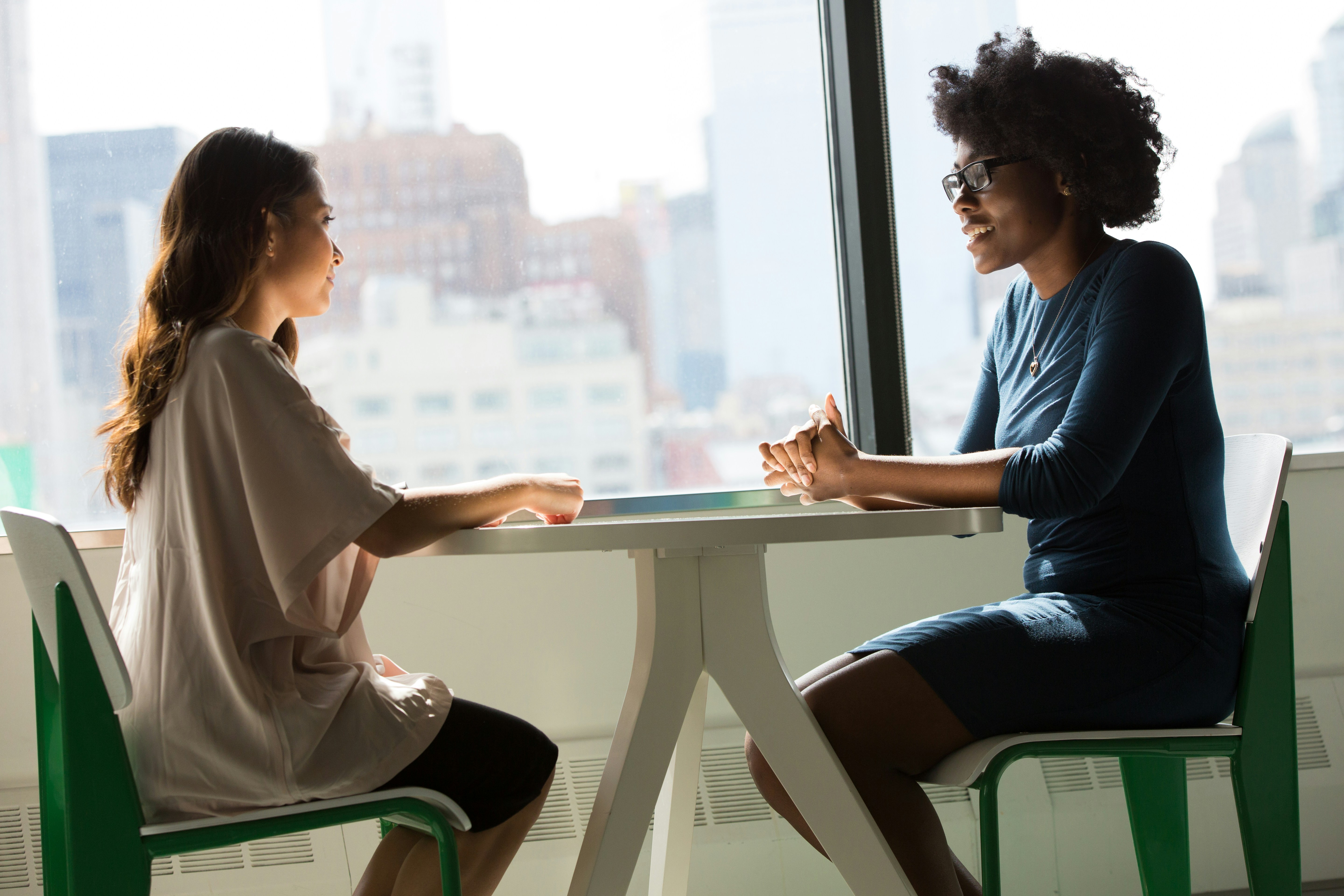 Two woman sat opposite each other on a table having a conversation